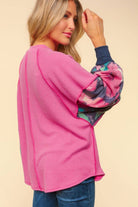 Woman modeling Sweet Pea Ribbed Top with magenta body and floral navy sleeves, showcasing oversized fit and bubble sleeves.