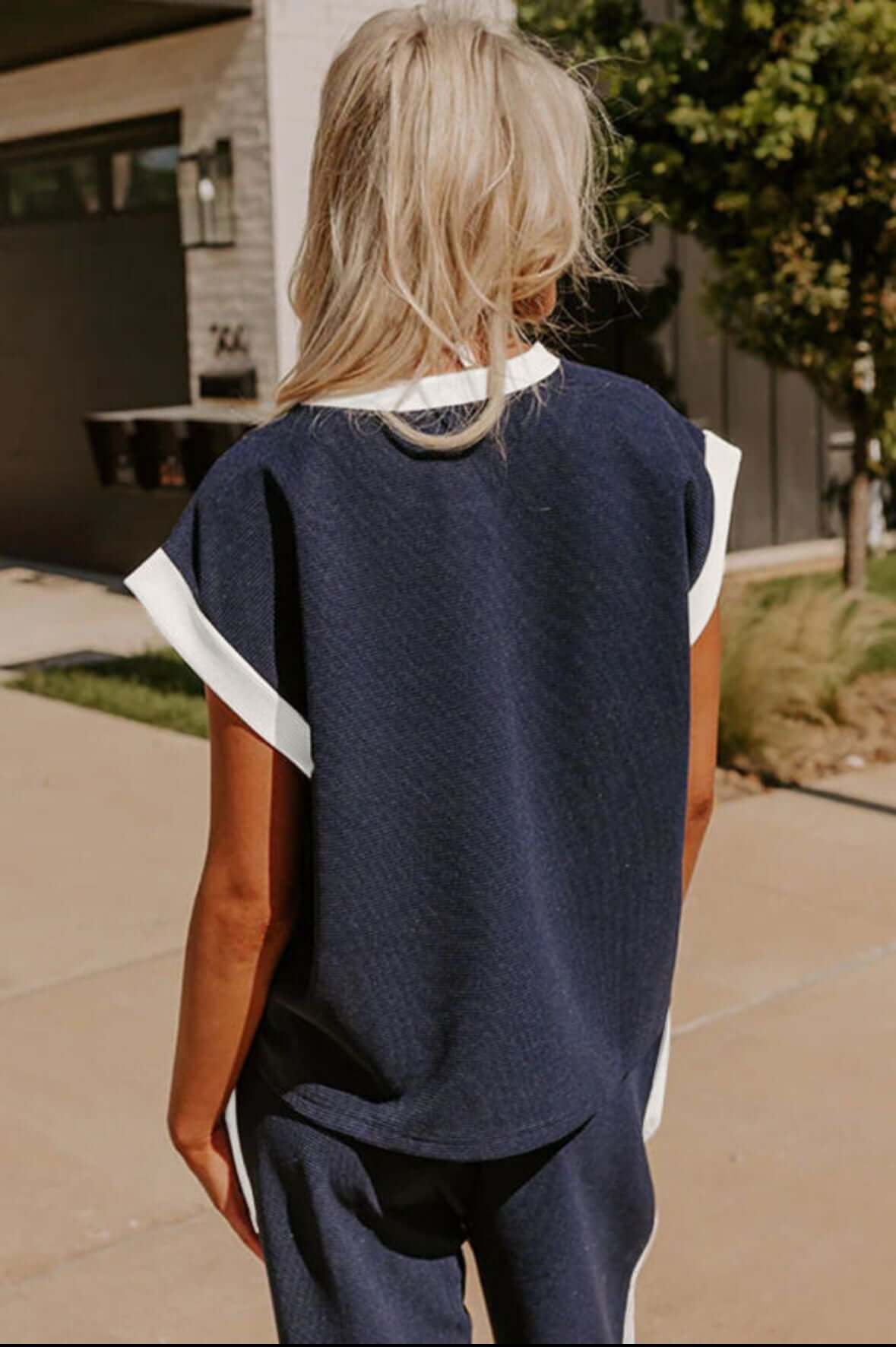 Back view of a woman wearing a navy blue two-piece pants set with white trim, showcasing a relaxed fit and cap sleeves.