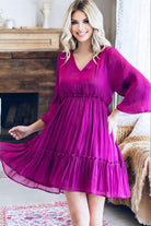 Magenta Bermuda Beauty Dress with v-neckline and balloon sleeves in crinkle shimmery fabric, worn by woman standing indoors.