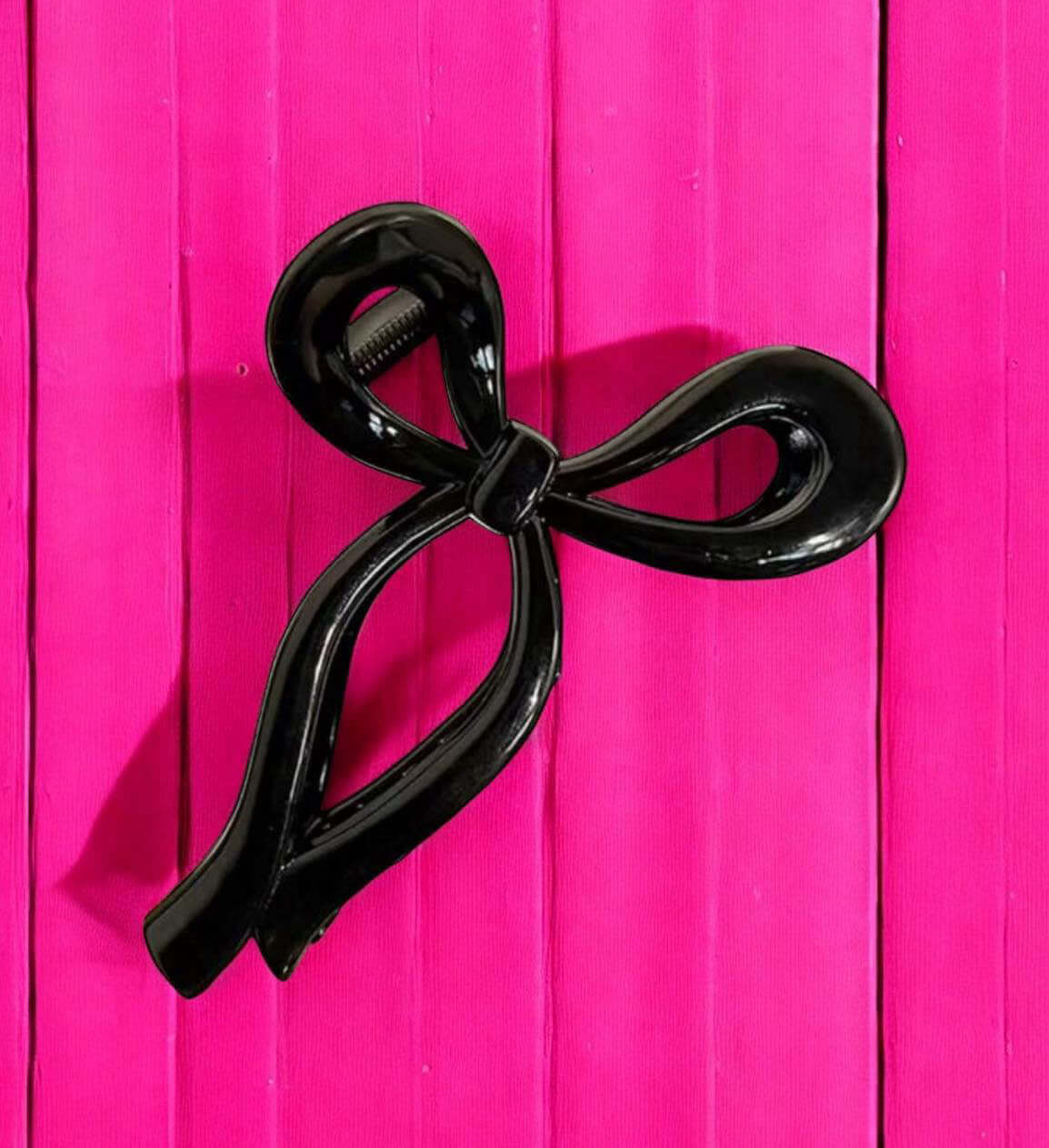 Black bow-shaped hair clip on a vibrant pink background for secure styling.