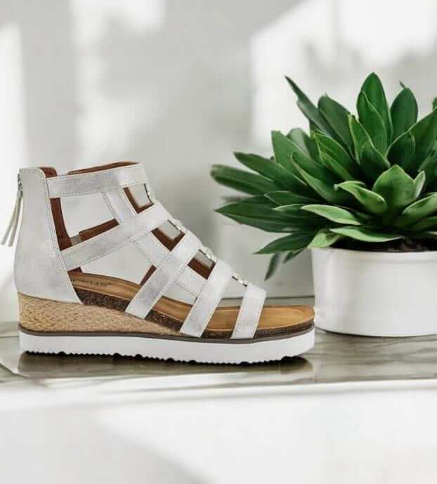 Corky's Caged Wedge Sandals in white with faux leather straps and a cork footbed, styled with a plant.
