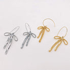 REFIEND RIBBON EARRINGS (2 colors) displayed in silver and gold with delicate bow-inspired designs.