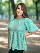 Woman wearing turquoise checkered Aqua Angles Top by Umgee with puff sleeves and relaxed silhouette in a park setting.