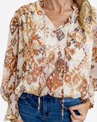 Woman wearing the GOLDEN GLOW TOP by Avara, featuring beige, brown tones, and smocked sleeves for an elegant look.