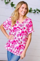 Model wearing a magenta and white geometric floral V neck top with banded sleeves, smiling against a floral backdrop.