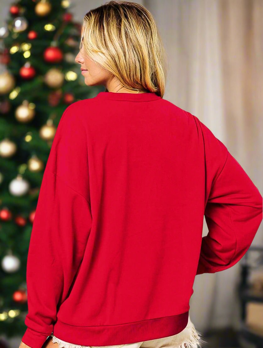 Woman wearing Santa Baby crewneck with Christmas tree in background.