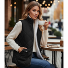 Model wearing a REVERSIBLE RETREAT VEST (black) while holding a coffee cup at an outdoor café.