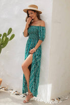 Woman in a teal off-shoulder slit maxi dress with a straw hat, enjoying a sunny day outdoors.