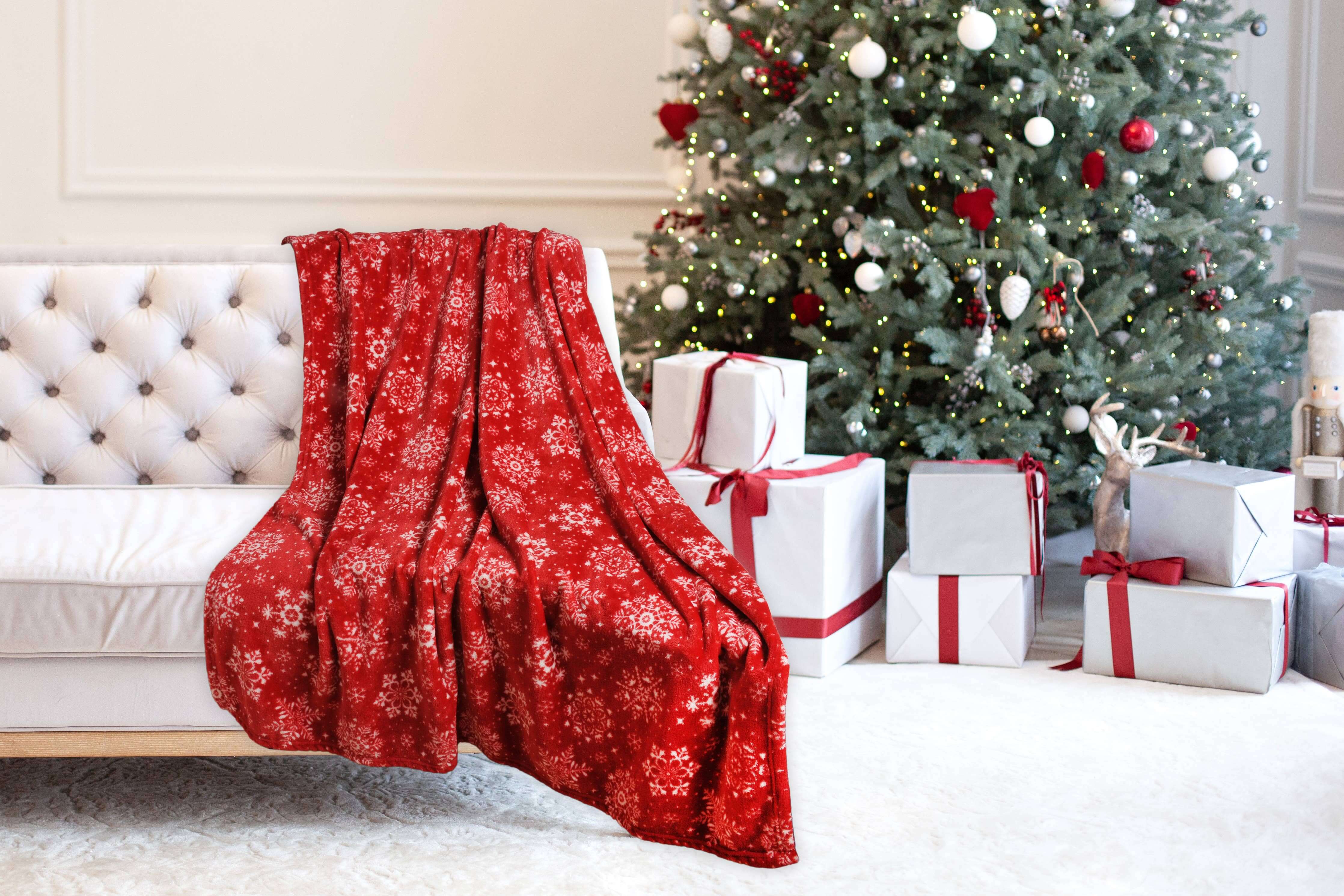 Festive red Christmas throw blanket on a couch beside a decorated tree and gifts, exuding holiday cheer and warmth.