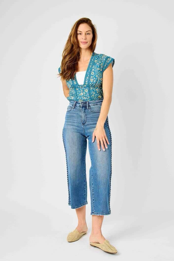 Woman wearing Judy Blue Braided Betty wide leg jeans with braided side detail, styled with a blue top and beige shoes.