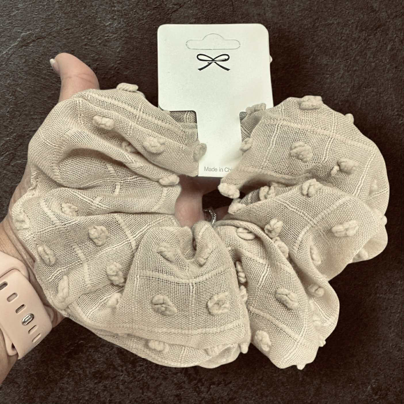 Cloud Comfort Scrunchie in light beige, featuring pompom texture and held on a hand, perfect for stylish hair accessories.