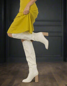 White knee-high boots with high heel by Oasis Society, styled with a yellow dress, embodying fashion-forward elegance.