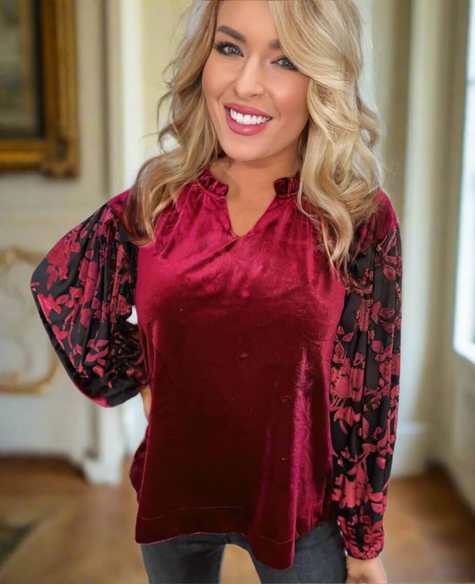 Woman wearing burgundy velvet top with black lace sleeves, V-neck, and ruffled collar from Umgee.