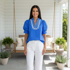 Model wearing BRIGHT FUTURE TOP - Entro in blue with embroidered V-neck, paired with white pants for effortless style.
