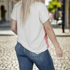 Back view of woman in floral patch top and jeans walking on cobblestone street, showcasing stylish casual wear.
