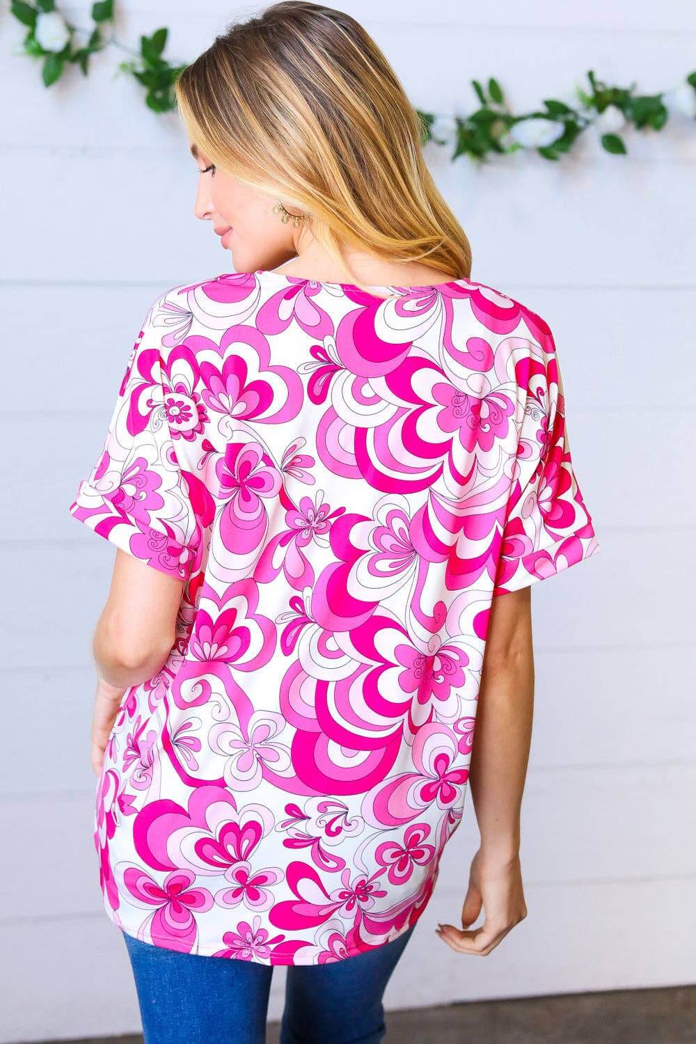 Back view of a woman wearing a magenta and white floral V neck top with banded short sleeves.