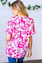 Back view of a woman wearing a magenta and white floral V neck top with banded short sleeves.