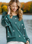 Woman wearing teal green sweater with star pattern, smiling by a lake in autumn.