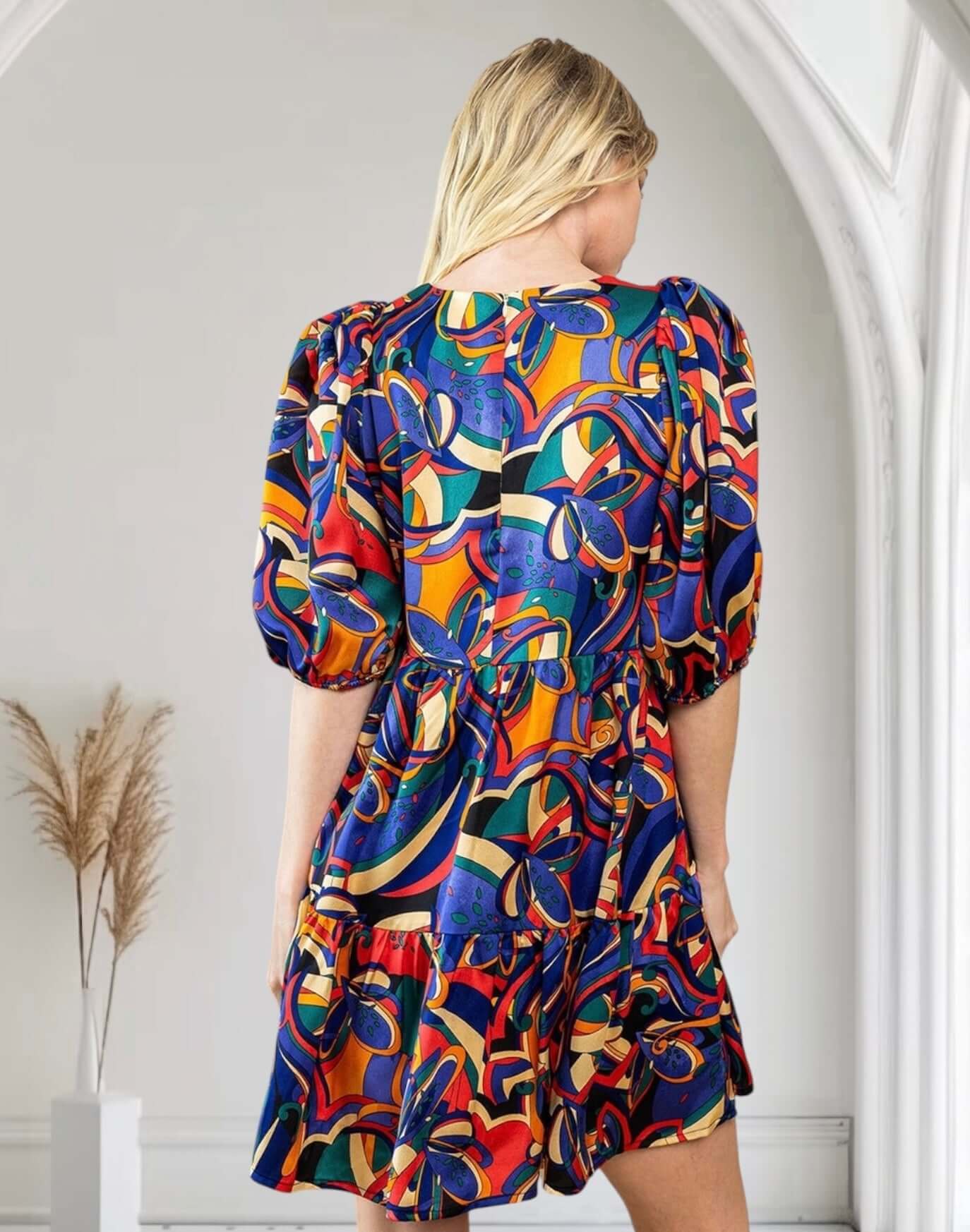 Woman wearing vibrant abstract print dress by TCEC, back view, puff sleeves, in stylish interior setting.