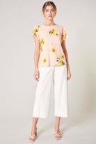 Model wearing DAISY MARIE TOP in blush yellow with white cropped pants, showcasing a chic spring look.