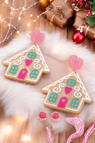 Gingerbread house earrings with festive colors and heart accents on a cozy holiday backdrop. Perfect for Christmas celebrations.