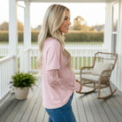 Woman wearing SIMPLY ENCHANTED TOP (pink) with lace sleeves, smiling on a porch.