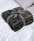 Folded LUXE DREAMS THROW BLANKET in dark charcoal and forest green with ribbon on a bed. Perfect for cozy nights in.