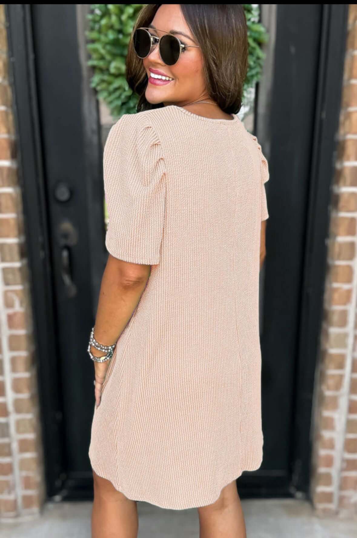 Back view of woman wearing beige Carefree Spirit Dress with puff sleeves and pockets, styled with sunglasses.
