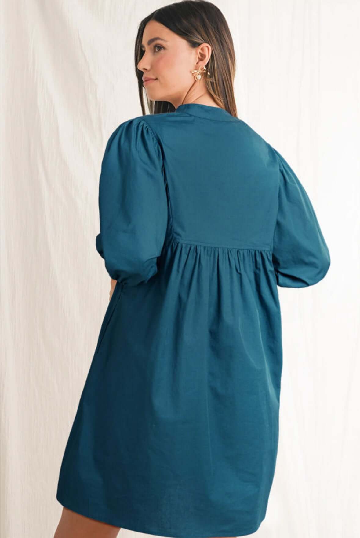 Model wearing the Aurora Dawn Dress, a teal mini dress with puff sleeves and a playful back detail.