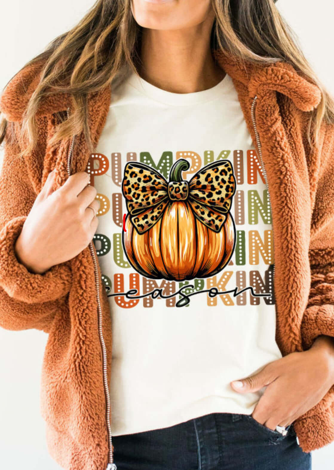 Woman wearing a cozy jacket showcasing the PUMPKIN PARTY TEE with a decorative pumpkin and bow design.