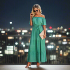 Woman in a green polka dot maxi dress, styled off-the-shoulder with ruffles and a belt, perfect for casual occasions.