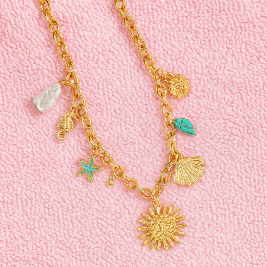 Golden Sunseeker Charm Necklace with pearls, seahorse, starfish, and seashells on a pink background.