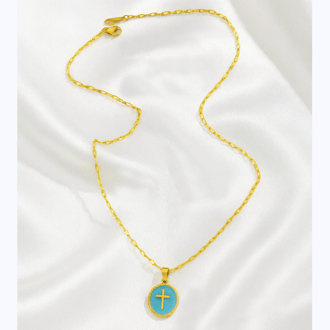 Gold-tone necklace with teal enamel cross pendant on satin background.