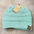 Teal C.C. Beanie with suede patch on fluffy background, showcasing cozy knit design.