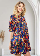 Woman wearing ART FUSION DRESS by TCEC with vibrant abstract print, perfect for any occasion, standing in stylish interior setting.