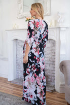 Woman wearing floral maxi dress standing by elegant white fireplace.