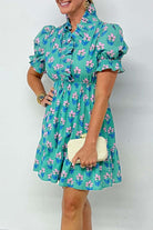 Woman wearing Ruffled Romance Dress in aqua with floral print and ruffled sleeves, holding a clutch.