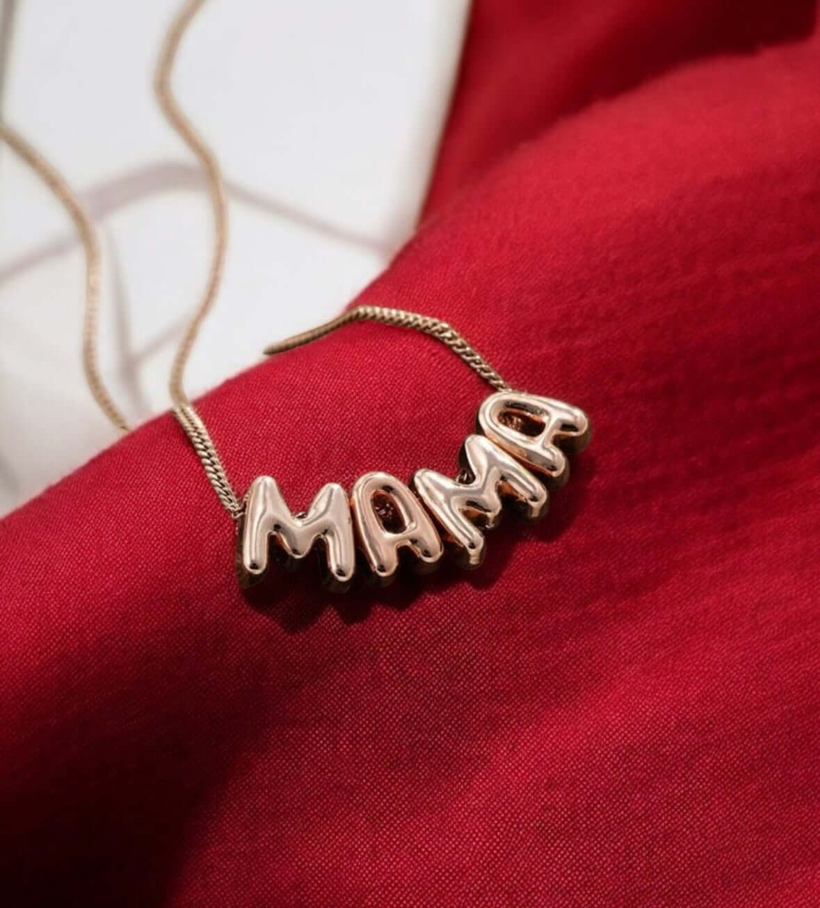 Bubbly Mama Necklace in rose gold tone on red fabric, featuring a bold 'MAMA' charm.