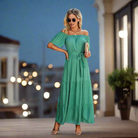 Woman in green ON THE DOT MAXI DRESS with off-shoulder style, playful ruffles, and a belted waist, perfect for casual outings.