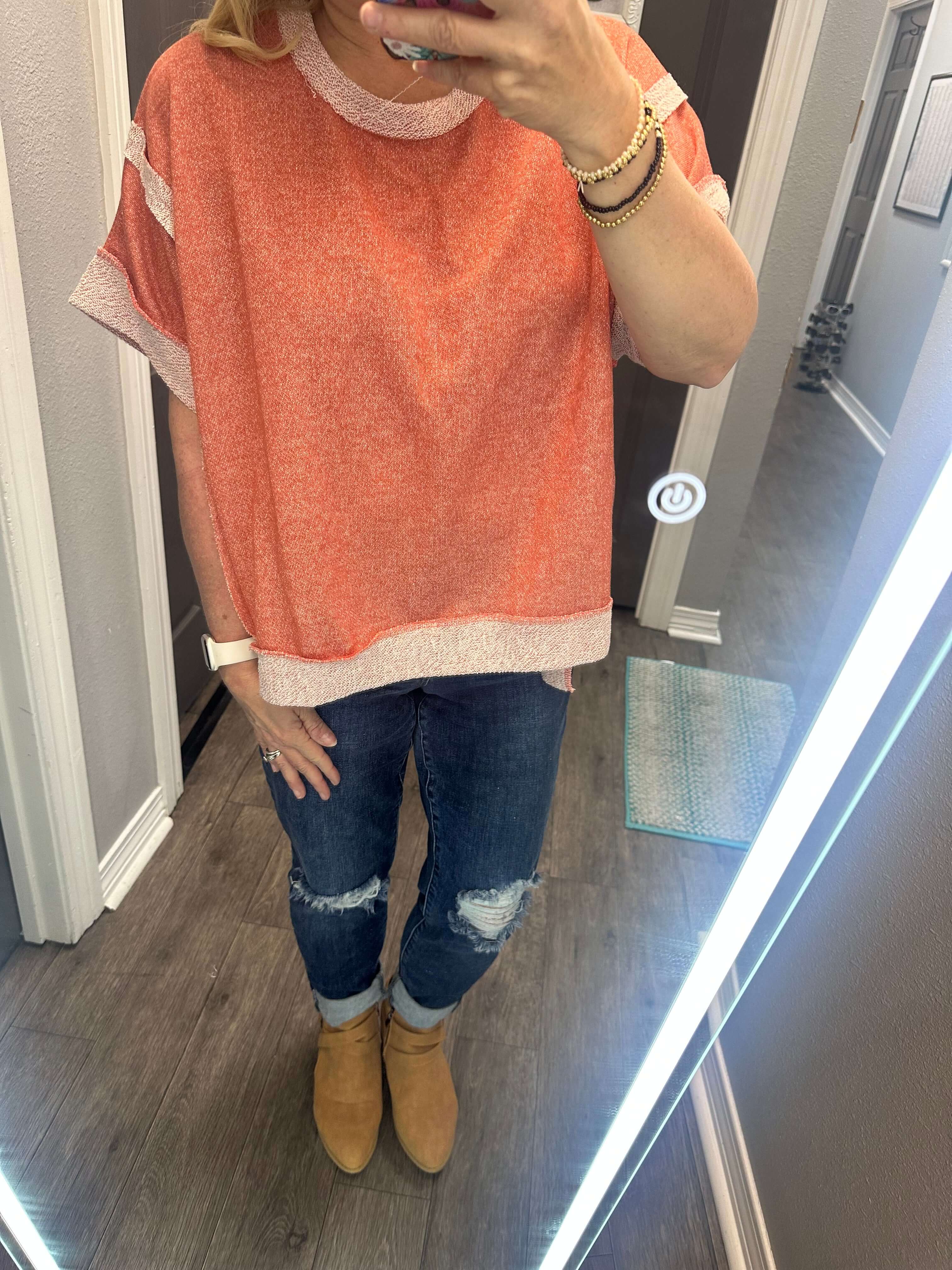 Woman wearing a casually cute peach passion top paired with distressed jeans and stylish ankle boots.