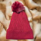 Scarlet Pearl Beanie, dark red cable knit hat with scarlet pearls, fluffy pompom, on faux fur background. Cozy, elegant winter accessory.