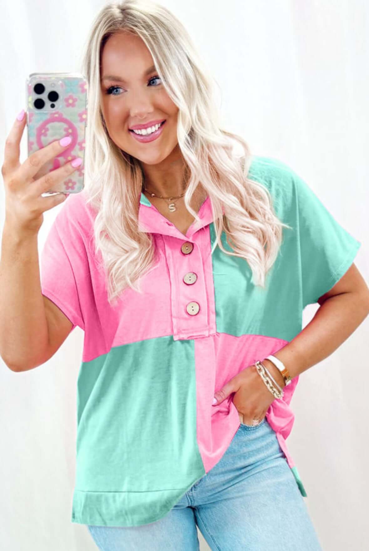 Woman smiling in a color-blocked pink and teal top with buttons, showcasing casual summer style.