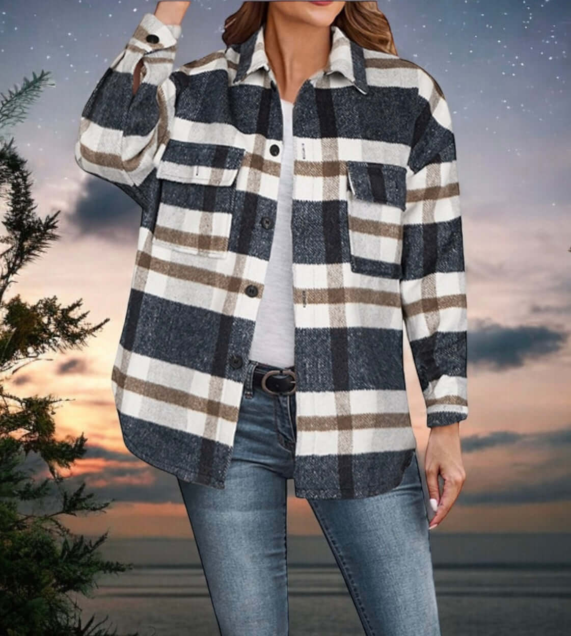 Woman wearing a cozy plaid Woodland Trail Shacket by Melody, styled as a jacket, against a scenic sunset background.