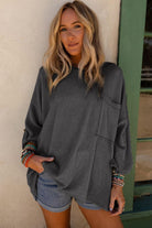 Woman wearing charcoal gray oversized top with ribbed knit fabric and roll-tab sleeves, styled with denim shorts and bracelets.