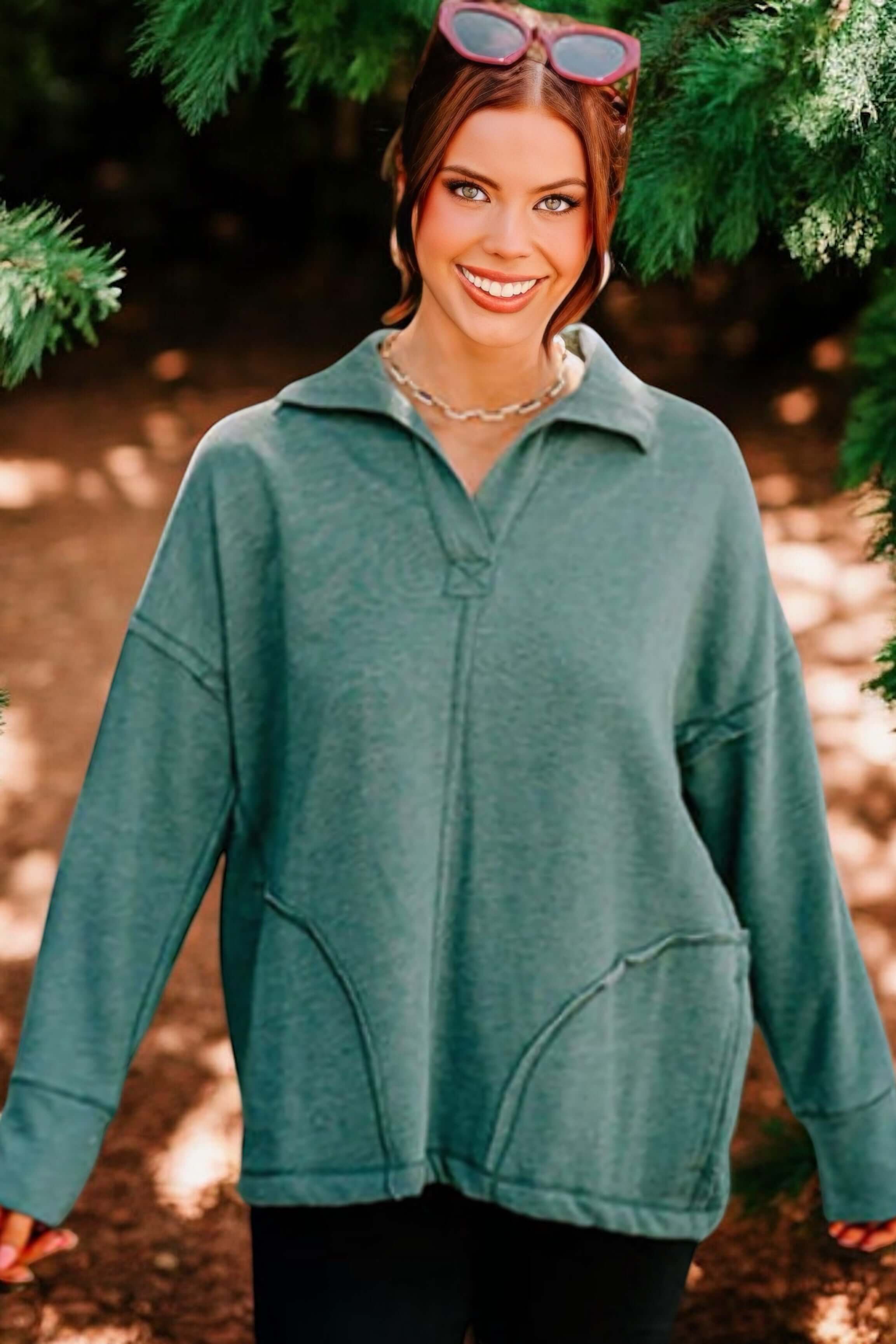 Woman smiling in a stylish evergreen pullover sweater, showcasing a relaxed fit and cozy vibe amidst greenery.