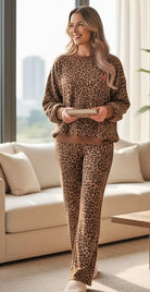Woman in SPOT ON COZY SET featuring leopard print sweater and pants, relaxing in a modern living room.