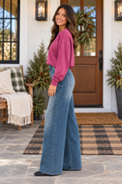 Woman in pink sweater wearing JUDY BLUE - LIZA palazzo jeans, standing on porch with festive decorations.