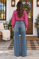 Back view of a woman in JUDY BLUE - LIZA Palazzo Jeans with a pink sweatshirt, standing on a porch.