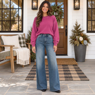 Model wearing JUDY BLUE - LIZA palazzo jeans with a pink sweatshirt outside a stylish home.