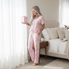 Woman in soft SUGARPLUM SANTA PAJAMA SET holding a gift, showcasing cozy holiday vibes in a bright living room.